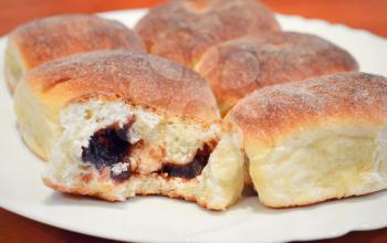 Buns filled plum jam. Bun with first missing bite on white plate.