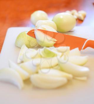 Closeup of orange ceramic knife slicing the fresh onion into small pieces on cutting board.