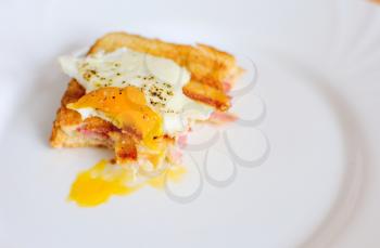 Leftover of ham and cheese toast with fried egg on top with missing bites.