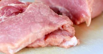 Raw pork meat slices on white cutting board.