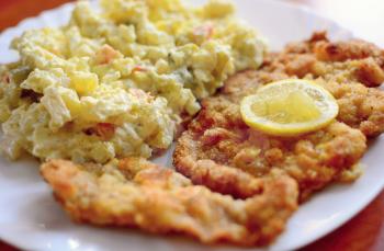 Traditional fried pork schnitzel with Czech potato mayonnaise salad and lemon slice on top.