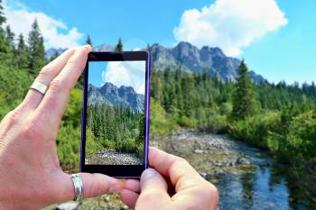View over the mobile phone display during shooting nature of High Tatras. Holding the mobile phone in hands and taking a photo, focused on mobile phone screen.