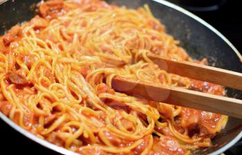 Cooking the spaghetti with red tomato sauce and sausage. Stirring spaghetti by the wooden tongs in pan.