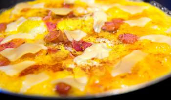 Frying ham and eggs with cheese, sausages and pepper in pan sprinkled by caraway seeds closeup.