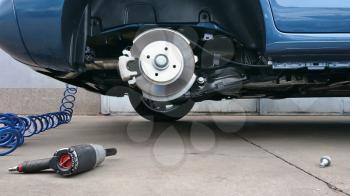 View of a car disc brake and pneumatic air screwdriver on the ground during tyre replacement. Car maintenance.