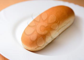 Closeup of a soft plain hot dog bun on a white plate.