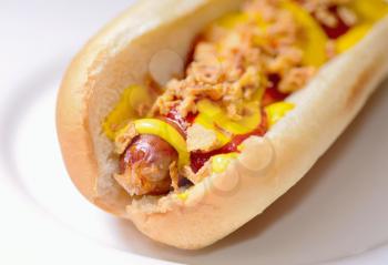 A hot dog in a plain soft bun with mustard, ketchup and fried onion.