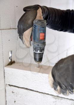 The bricklayer using a battery screwdriver for drilling a screw into a concrete aerated blocks wall. 