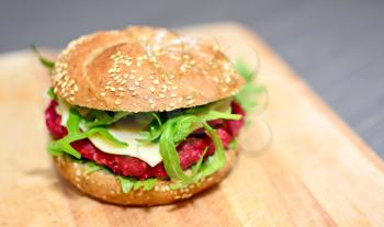 Closeup of beetrot burger with grilled arugula on wooden plate.