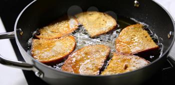 A frying of bread in hot oil in black pan close up.