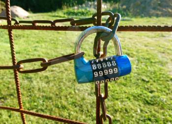 Closeup of a locked gate to a garden with a code lock and chain.