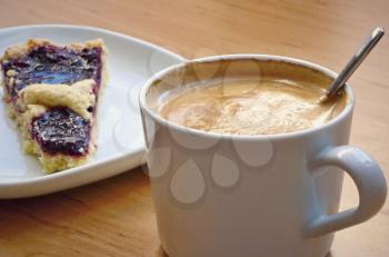 Close up of a white cup with coffee and cake on the plate in background.