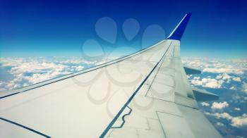 Classic passenger view of wing and sky with clouds from an airplane window during flight.