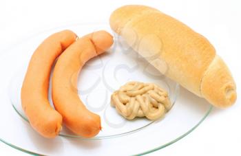 A plate of two frankfurter sausages with bread roll and mustard over white background. 