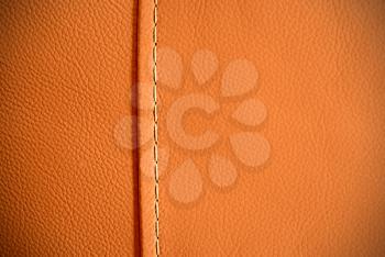Full frame background texture of pebbled orange leather with one seam thread.