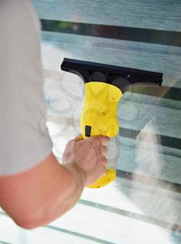 Cleaning window with cordless electrical vacuum cleaner. Man holding and using vacuum cleaner.
