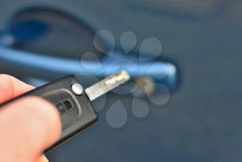 Closeup of hand holding a remote key unlocking the blue car.