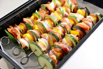 Pan full of metallic skewers with uncooked raw pork meat and vegetables ready for baking.