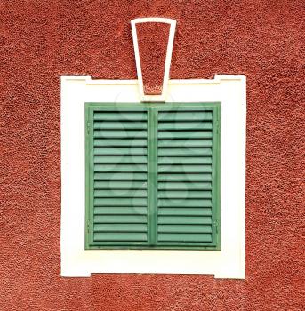 Ancient baroque window with white frame and closed green wooden exterior shutters in red facade.