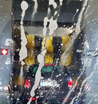 A car is washing in a car wash, a view through the wet windshield. The brushes washing a car in a car wash.
