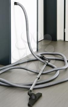 Long central vacuum cleaner hose laid on the grey floor in the room. Hose of central vacuum cleaner plugged into a wall inlet valve socket.