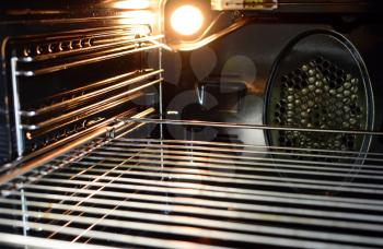 A view of the inside of an empty oven with lighting bulb and a wire rack.