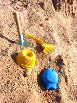 Close up of toy shovel, rake and plastic cake and fish on the sandbox sand.