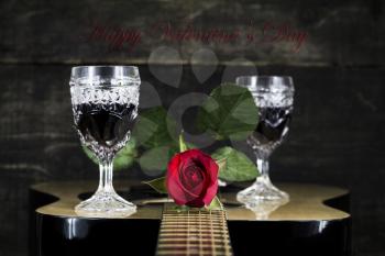 Red Rose and Wine Glasses Resting On Acoustic Guitar With Sign Happy Valentine's Day