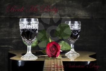 Red Rose and Wine Glasses Resting On Acoustic Guitar With Sign Rock Me Baby. Valentine's day concept