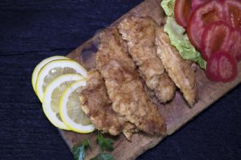 Breaded Chicken Meat With Salad And Lemon Resting On a Rustic Wooden Board 