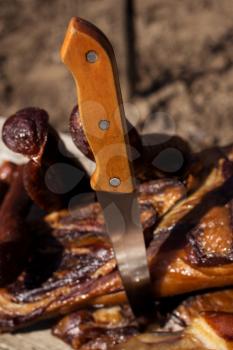 Butcher's Knife Stabbed In The Smoked Bacon With Dried Sausages On A Rustic Wooden Surface. Delicious Domestic Food