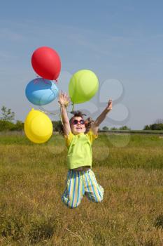 happy little girl jumping with balloons on meadow
