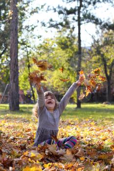 happy little girl throws leaves
