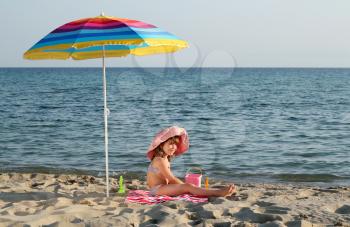 happy little girl sitting under sunshade on beach