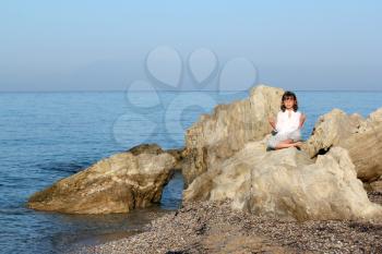 little girl sitting on a rock by the sea and meditate