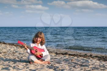 little girl sitting on beach and play guitar