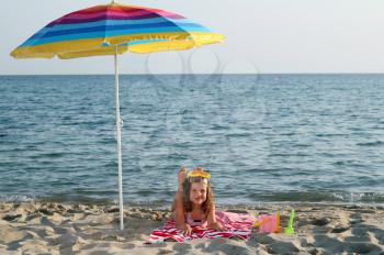 little girl with diving mask lying under sunshade on beach