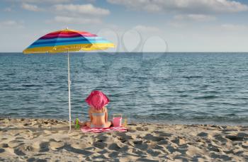 little girl with hat sitting under sunshade on beach