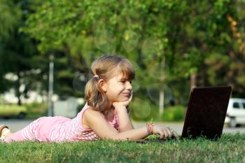 little girl lying on grass with laptop