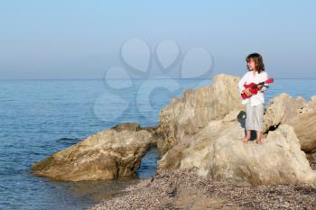little girl with guitar standing on a rock