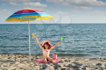 happy little girl with hands up sitting under sunshade on beach