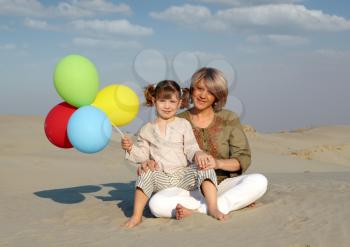 happy mother and daughter with colorful balloons sitting on sand