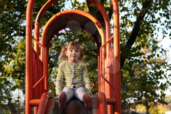 beautiful little girl sitting on playground slide