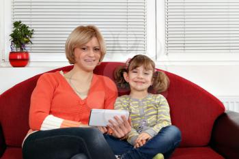 happy mother and daughter sitting on bed with tablet pc