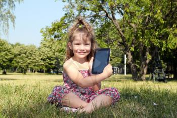 little girl with tablet sitting on grass