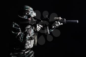 Bearded Special forces United States in Camouflage Uniforms studio shot half length black background, backlit. He is shooting killing enemy, pointing the rifle