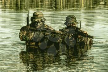 Pair of soldiers in action during river raid in the jungle waist deep in the water and mud and covering each other