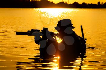 Silhouette of special forces with rifle in action during raid crossing river in the jungle waist deep in the water