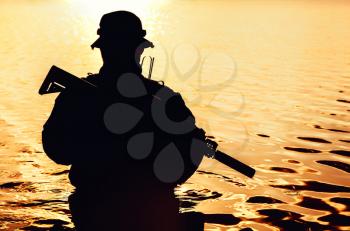 Silhouette of special forces with rifle in action during river raid in the jungle waist deep in the water. Front view, half length