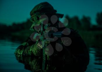 Silhouette of special forces with rifle in action during river raid in the jungle waist deep in the water. Under cover of darkness